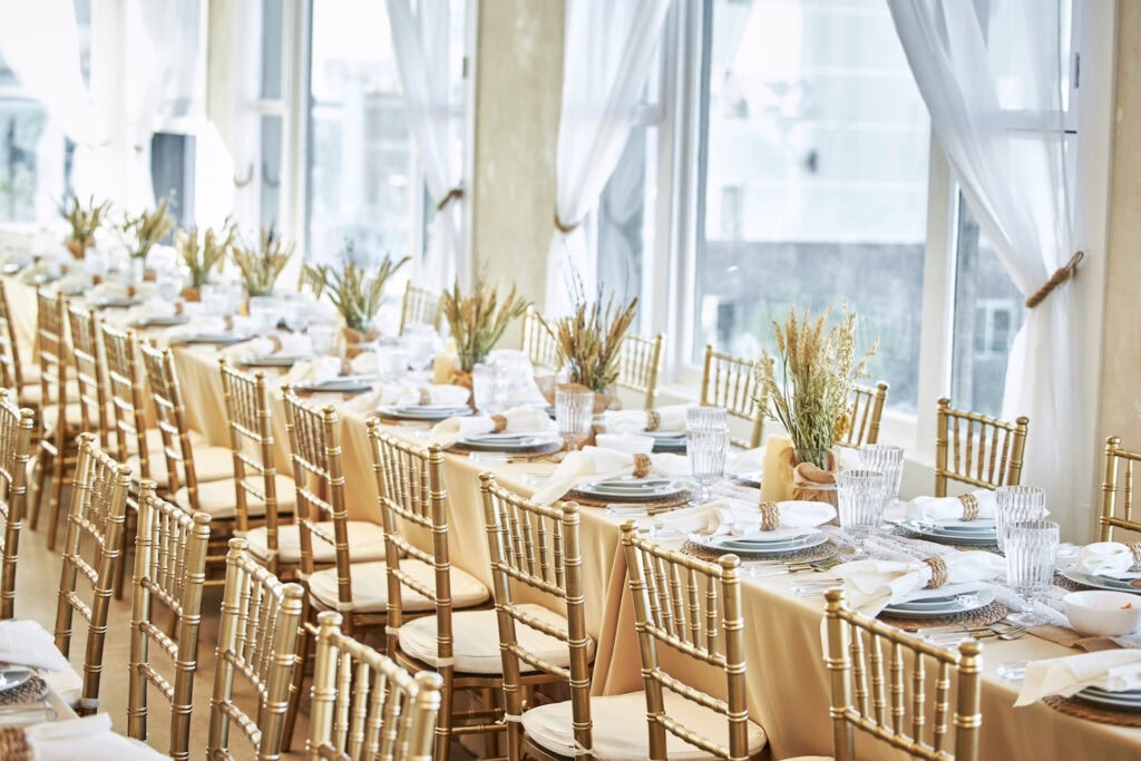 Gold chairs line a long reception table decorated with simple centerpieces