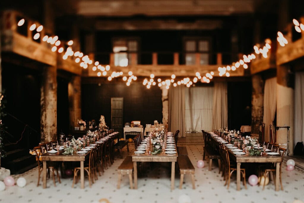 Long, wooden tables set up in rows under string lights in a lodge-like reception space