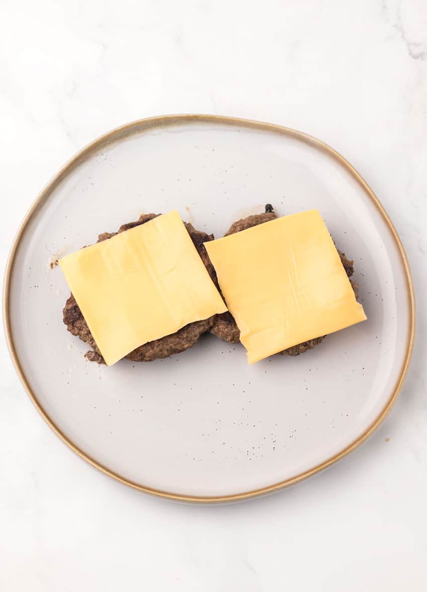 two grilled hamburger patties topped with slices of American cheese on a gray plate