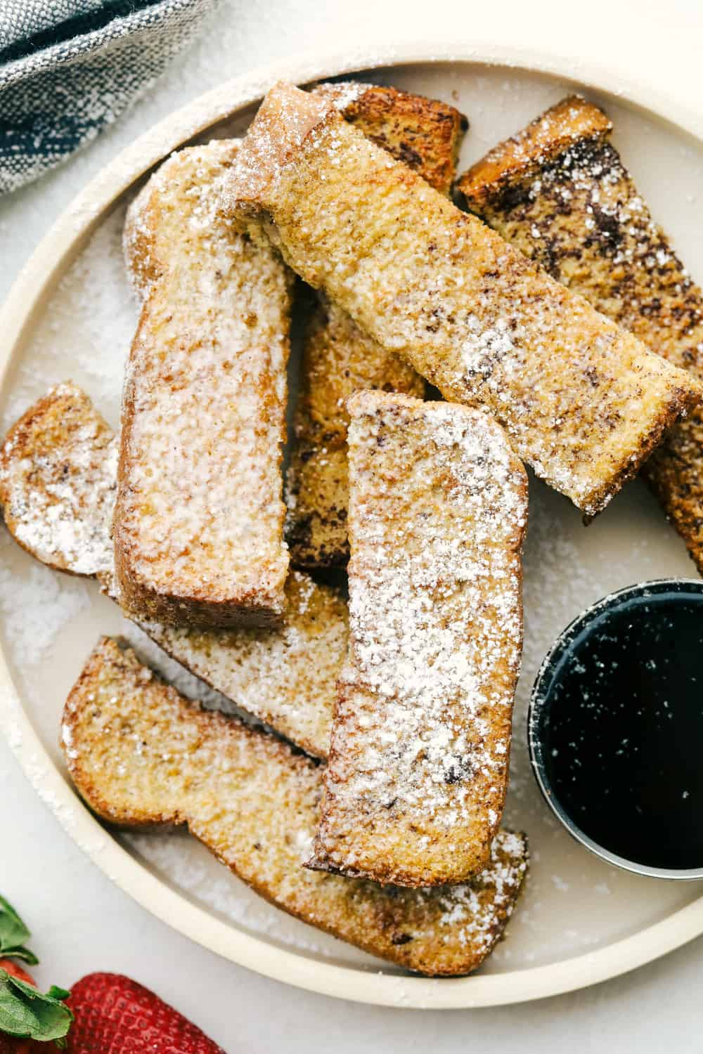 Air Fryer French Toast Sticks are a super fun fast way to make breakfast in the morning. Coated in a vanilla and cinnamon egg mixture, these fry up absolutely amazing! Air fryer french toast sticks layered on a plate with powdered sugar
