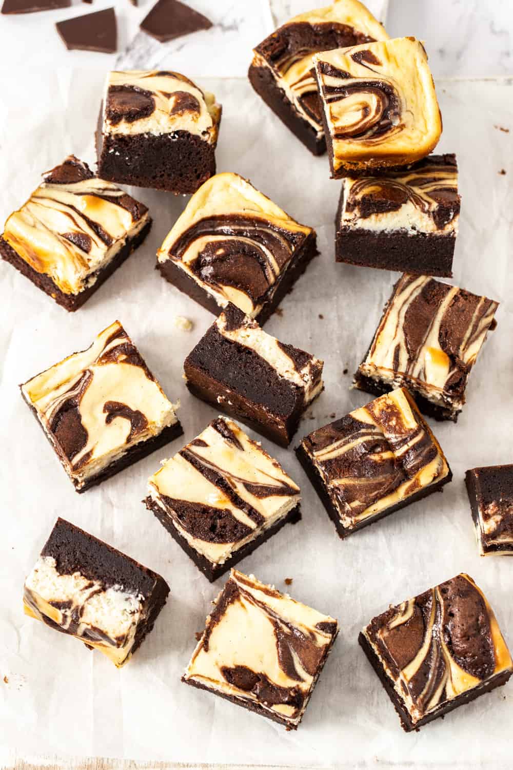 Super fudgy brownies, topped with a layer of creamy cheesecake, these deliciously indulgent Cheesecake Brownies are easy to make in just two bowls. Top down view of a batch of cheesecake topped brownies on a sheet of baking paper.