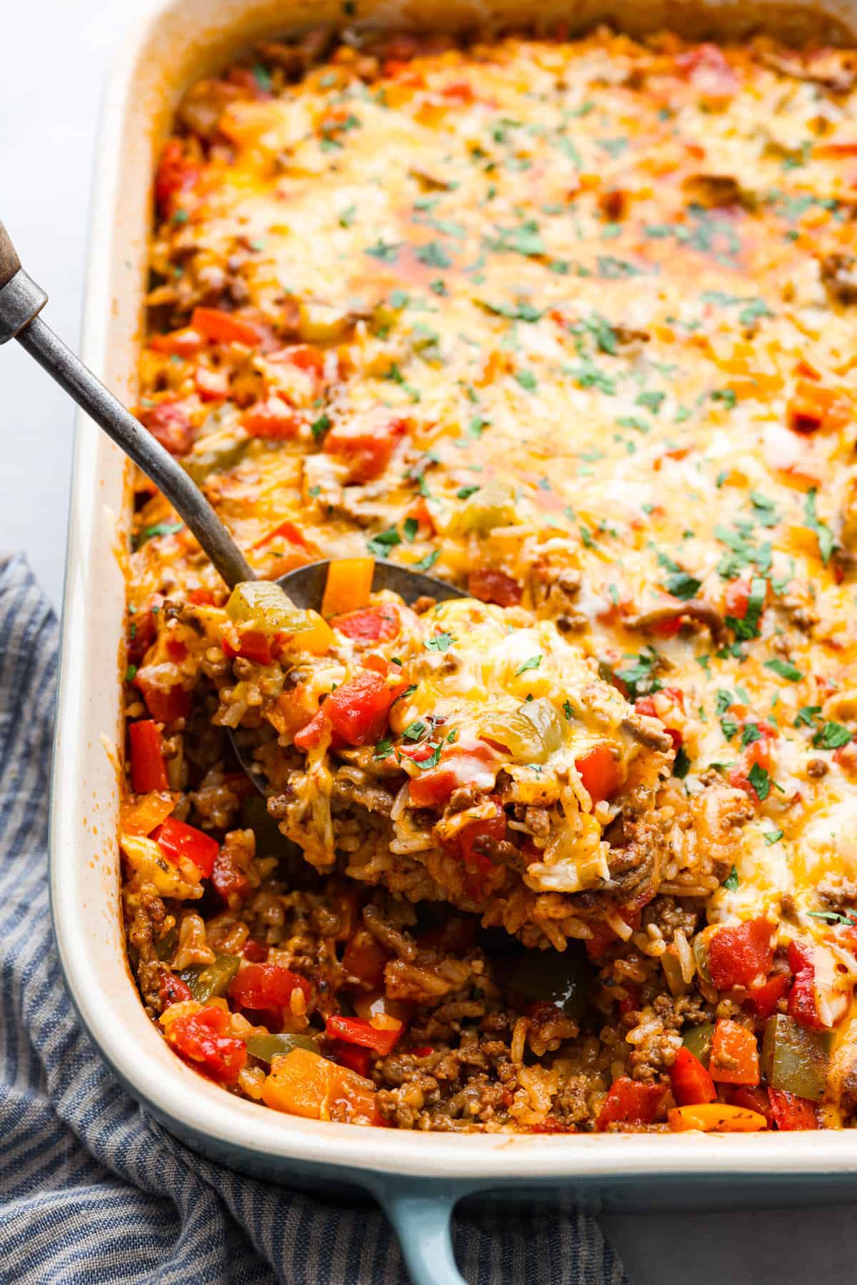 All the hearty, flavorful goodness of a stuffed pepper in one easy-to-make casserole! Stuffed pepper casserole is easy, cheesy, and packed to the brim with delicious seasoned rice and vegetables. Closeup of stuffed pepper casserole on a metal serving spoon.