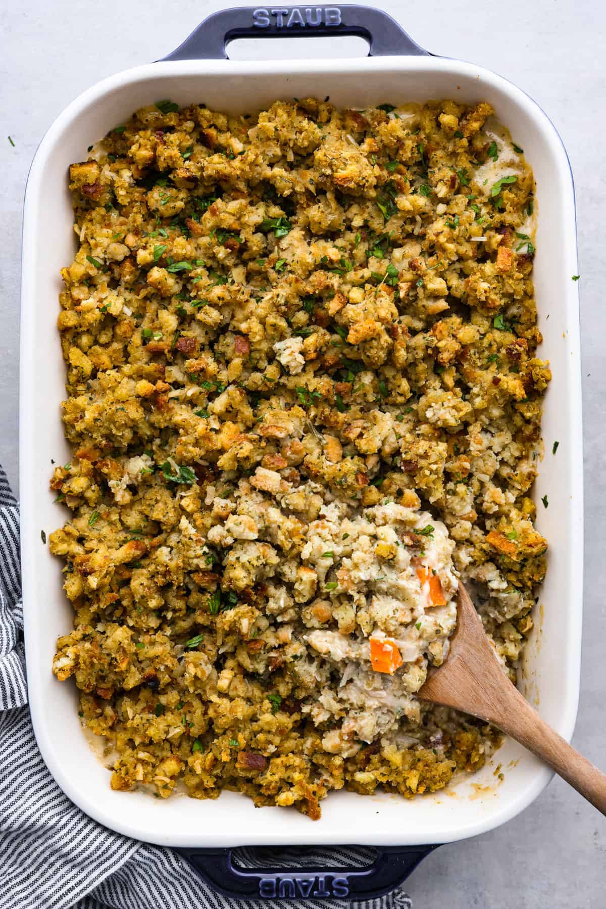 A delicious, hearty casserole made with stuffing mix, shredded chicken, vegetables, and all the tasty seasonings. Chicken and stuffing casserole is a fun twist on a classic dish and the perfect addition to your Thanksgiving lineup! Top-down view of baked chicken and stuffing casserole in a blue and white staub pan.