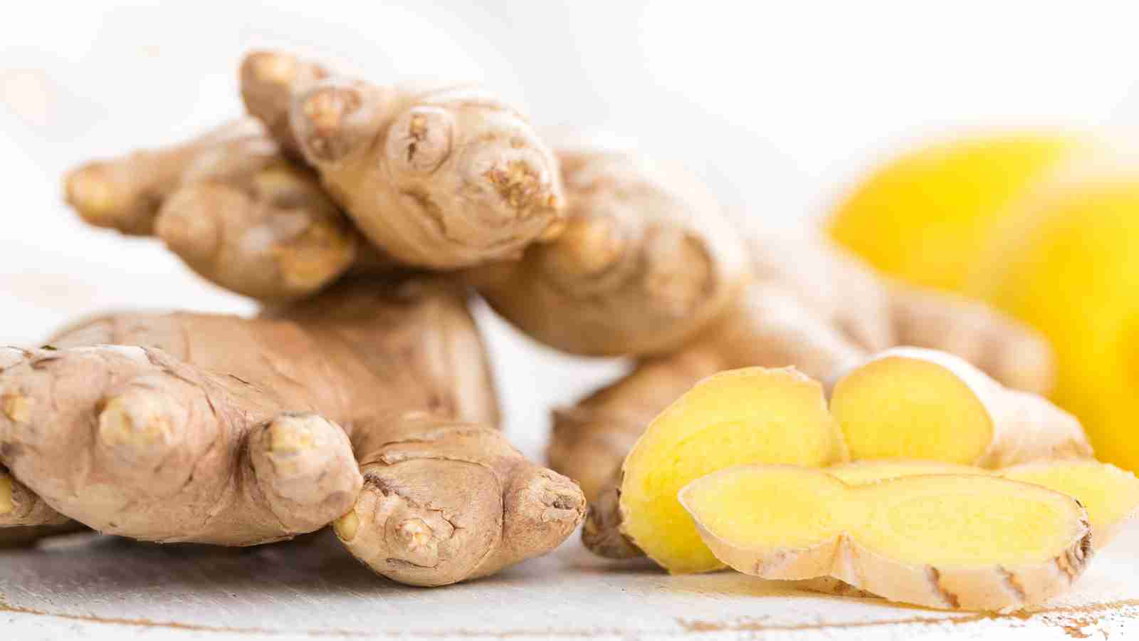 A stack of whole ginger roots next to several slices of ginger.