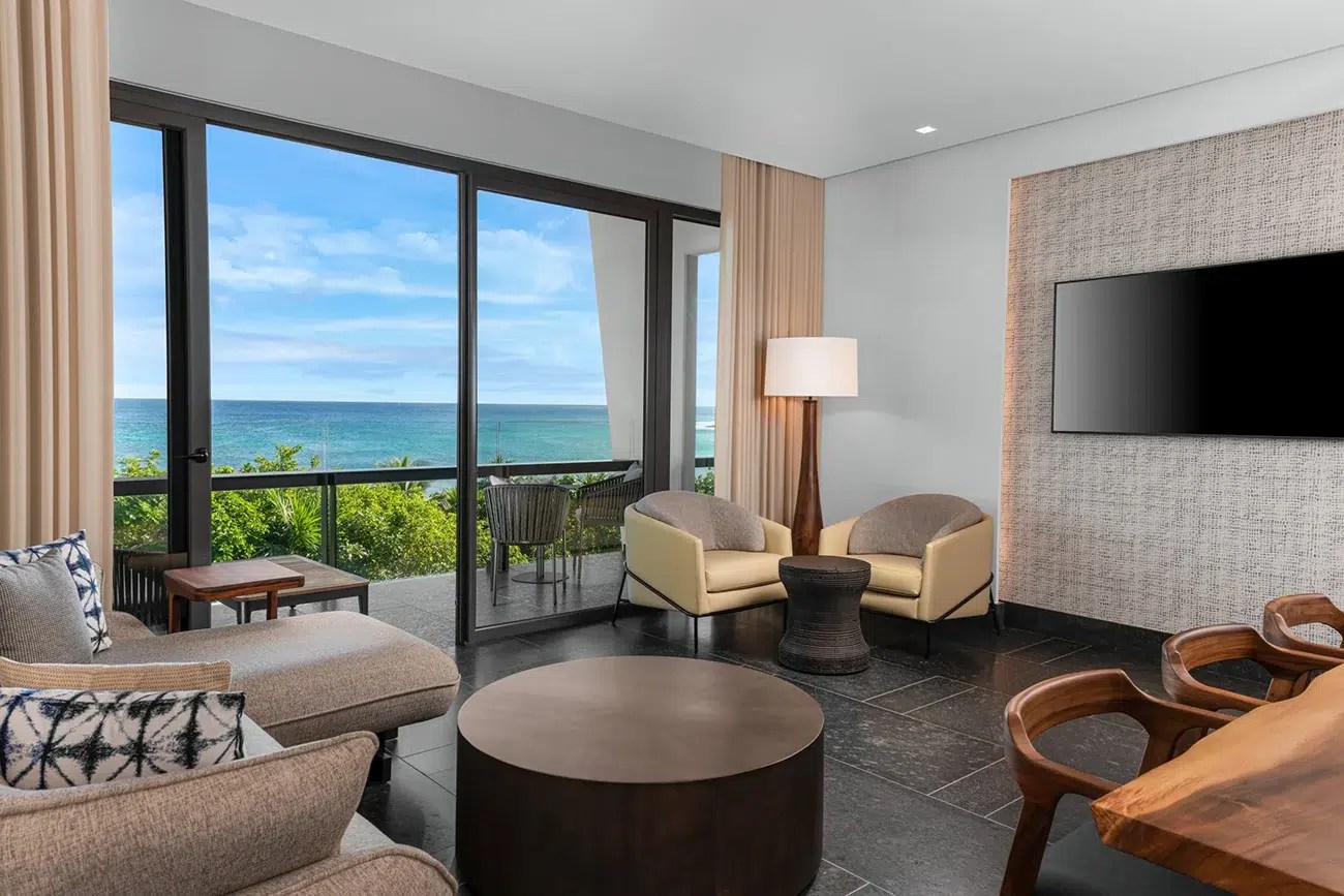Luxury oceanfront suite with panoramic floor-to-ceiling views, modern lounge seating, and a private terrace overlooking the turquoise sea. Luxury oceanfront suite with panoramic floor-to-ceiling views, modern lounge seating, and a private terrace overlooking the turquoise sea.