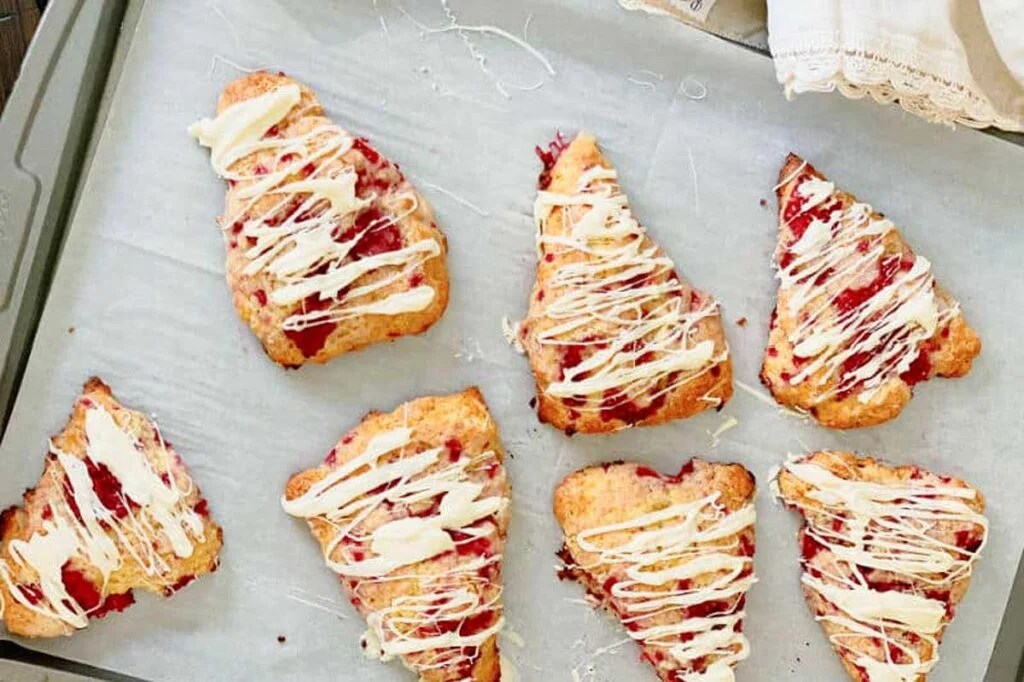 Raspberries and white chocolate scones on a baking sheet with fresh raspberries