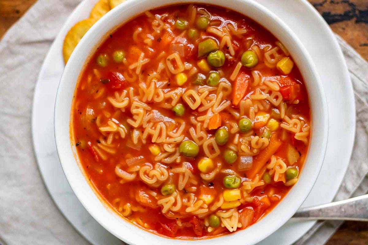 A bowl of noodle soup with frozen mixed vegetables.