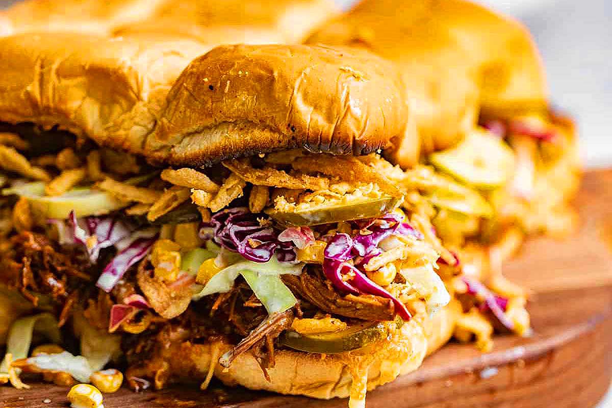 A slider-sized pulled pork sandwich on a rustic wooden cutting board.