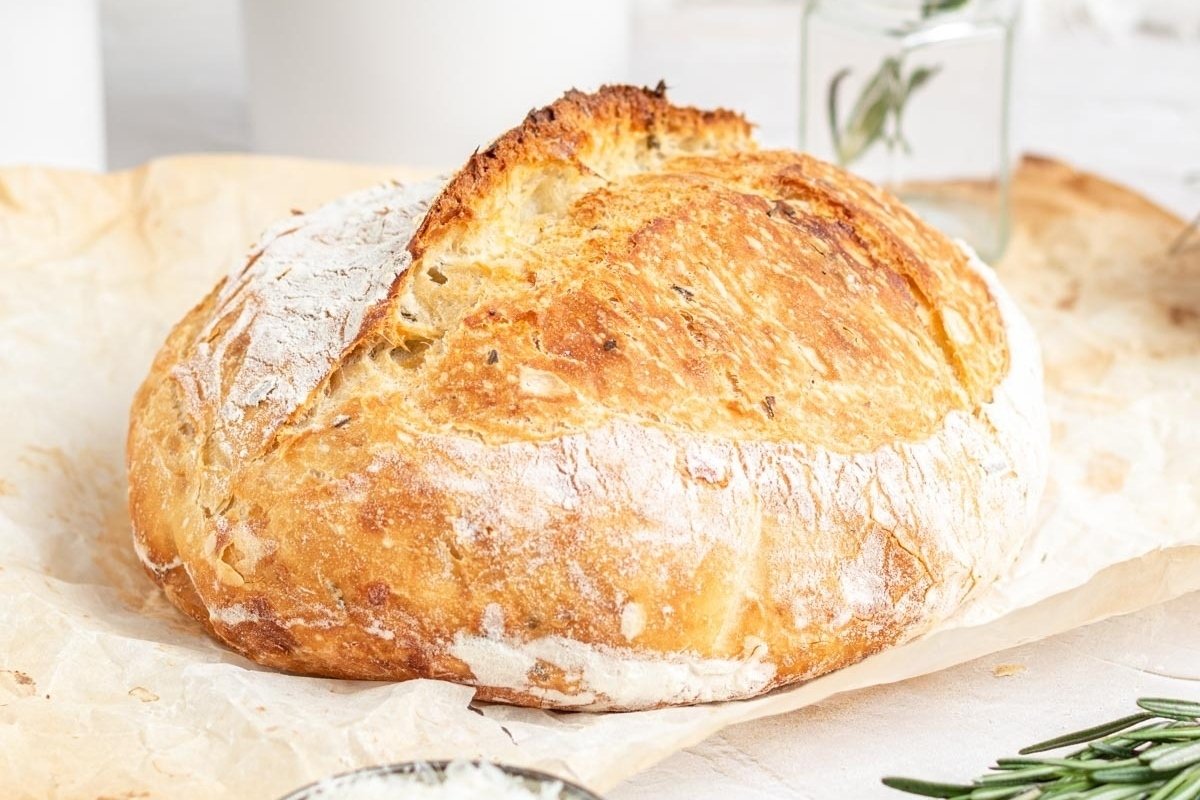 A loaf of bread with rosemary sprigs on a piece of paper featuring bread recipes.
