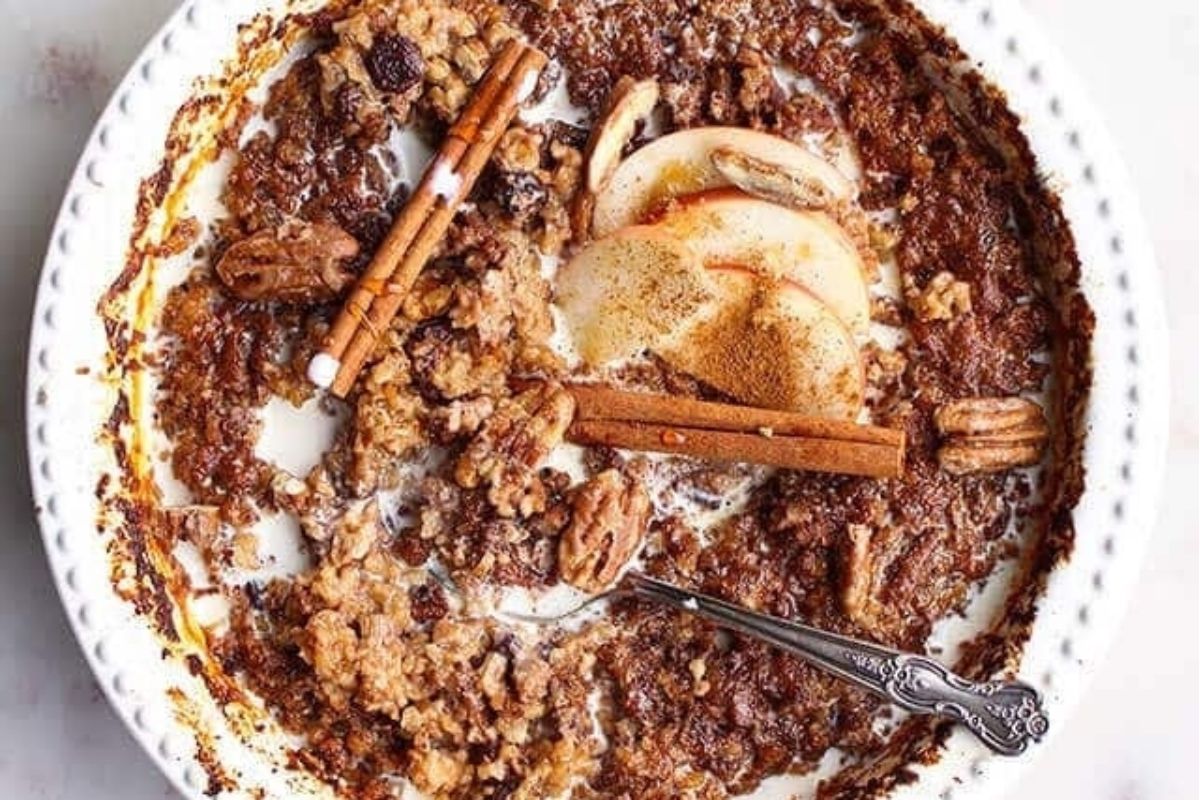 An oatmeal recipe topped with cinnamon sticks, served with a spoon.