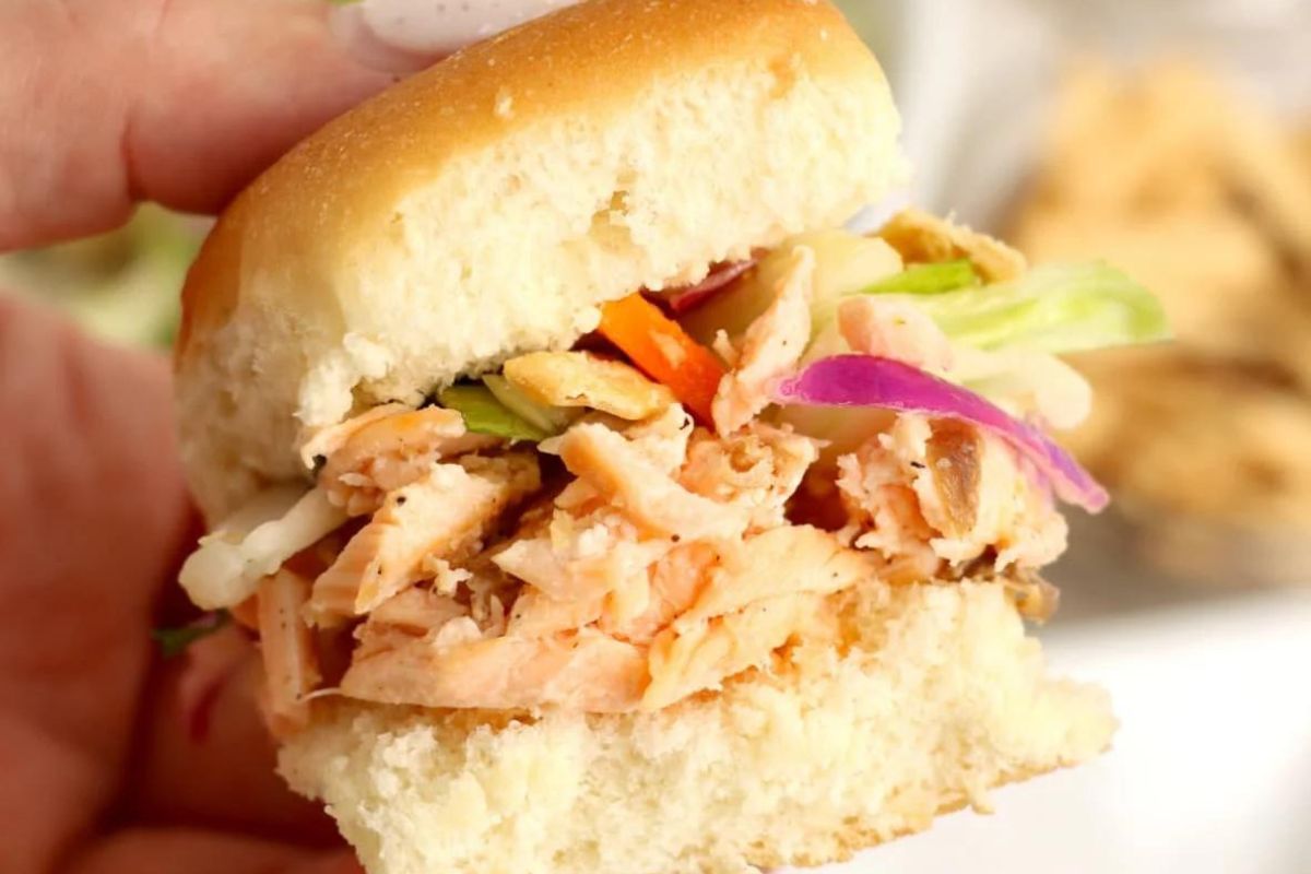 A hand holding a half-eaten slider with shredded meat and vegetables.